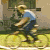 Animated sequence of a person in blue shirt and dark pants riding a bicycle, then walking with it through an outdoor setting.