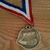A silver medal with red, white, and blue ribbon on a wooden background; text overlays change between frames.
