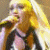 A pixelated image of a person with long blonde hair singing into a microphone, wearing a dark outfit on the left side and a pink top on the right side.