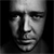 Black-and-white pixelated image of a human face with a neutral expression, showing eyes, nose, mouth, and forehead against a dark background.