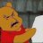 A pixelated close-up of a yellow bear wearing a red shirt, with a blurred background showing indistinct shapes and colors.