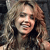 A pixelated close-up of a person with light brown hair, wearing a dark top, against a dark background with visible pixelation.