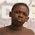 Pixelated close-up of a person with short dark hair, light brown skin tone, and a neutral expression against a blurred light-colored background.