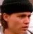 A pixelated close-up of a person's face wearing a dark cap, with visible ear and partial neck, against a light background.