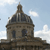 Pixelated image of a domed building with a spire under a light blue sky with scattered clouds.