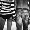 Black-and-white image of two people standing side-by-side, one in a striped top and shorts, the other in jeans with a belt, viewed from the waist down.