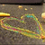 Pixelated static image with abstract swirling patterns in yellow, green, and pink against a muted brown background with scattered light spots.