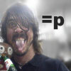 A person with long brown hair and a mustache wears a dark shirt, holding a colorful object while sticking out their tongue, with '=p' text on the right.
