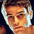Pixelated close-up of a person with light brown hair and fair skin, wearing dark clothing against a dark background.