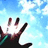 Pixelated hand with dark sleeve against light blue sky background, fingers extended upward.