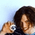 Pixelated image of a person with dark curly hair holding a camera against light blue background.