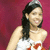 A woman in a white strapless dress with red accents and a silver tiara smiles against a solid red background.