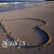 A heart-shaped sand drawing with a golden outline on a beach, featuring white text at the bottom left corner.