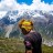 Pixelated static image of a person with a yellow head covering standing in a landscape with blue sky and green ground.