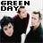 Pixelated static image with bold black text 'GREEN DAY' above three people in dark clothing against a light background.
