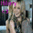 Pixelated image of a person with light hair and pink accents, wearing dark clothing against a blurred background.