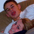 A pixelated image shows a person in a white shirt with brown hair, holding another person close against an outdoor background.