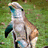 Pixelated image of a dolphin-like creature with light gray and brown coloring, blue eyes, and dark green fins against a blurred green background.