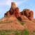 Pixelated landscape showing three reddish-brown rock formations against a light blue sky with sparse green vegetation at the base.
