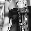 Black-and-white close-up of a person wearing a strapless dark dress with a large bow at the waist and multiple layered necklaces with circular pendants.