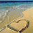 A beach scene with a heart-shaped sand drawing and ocean waves, alongside pixelated text reading 'OB Buddy' and other obscured words.