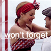 A woman in a red-and-white checkered halter top and red headband with a bow smiles while embracing a man in a flat cap against a light background.