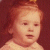 Pixelated image of a child with light brown hair and fair skin, wearing a white garment against a dark red background.
