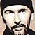 Static pixelated icon of a person's face with dark hair and mustache, wearing a black cap or head covering against a light background.