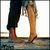 Two figures stand close together, one in dark pants and the other in light brown pants, with bare feet on a reflective surface.