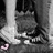 Black-and-white image of a person's lower legs and feet in sneakers, with pink heart shapes near the bottom left corner.