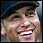 Pixelated close-up of a smiling person wearing a dark cap, showing teeth and facial features against a blurred background.
