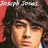 Pixelated close-up of a person with dark curly hair against red and brown background, text partially visible at top.