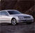 A silver sedan with dark-tinted windows is positioned on a dark asphalt surface against a dark background.