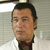 Static pixelated image of a person's head and shoulders in a white shirt with dark collar, set against light background.