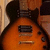 Pixelated image of an orange electric guitar with black accents and a dark brown neck, overlaid with blue text reading "Les Paul" in a bold, blocky font.