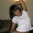 Pixelated image of a person with dark hair wearing a white shirt, raising one arm against a neutral background.