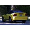 Yellow sedan with dark roof driving on road, rear view showing taillights and license plate, blurred background trees and road.