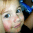 Pixelated close-up of a person with light hair and blue eyes, wearing a blue headband and dark clothing, with a blurred background.