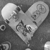 A grayscale heart-shaped icon with stylized text and symbols, featuring a central character design and circular emblems on the right side.