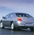 Pixelated image of a dark sedan with a person in red and white clothing standing beside it under a light blue sky.