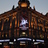Pixelated static image of a dark brown building facade with a central white rectangular feature and horizontal light blue bands at the bottom.