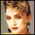 Pixelated static image of a woman's face with brown hair, red lips, and light skin tone against a muted gray background.