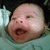 Pixelated close-up of a baby's face with mouth open, showing skin texture and background elements.