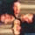 A pixelated image of a person with light skin and short hair holding multiple stacked objects, set against a dark background.