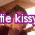Pixelated image of a person with brown hair and light skin, overlaid by purple text reading 'tie kiss' in white letters.