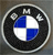Circular icon with black outer ring, silver border, and blue-and-white quadrant center; top arc contains partial 'M' text.
