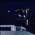 Pixelated dark blue background with a small light-colored circular object on the left, a stylized figure with white and gray limbs, and a light gray horizontal structure at the bottom.
