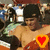 A shirtless person with dark hair and a cap stands in front of a crowd, with a heart symbol changing color in the foreground.