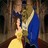 Two figures in formal attire embrace; one wears a yellow gown, the other a blue dress, against a dark background.