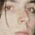 Pixelated close-up of a person's face with light skin tone, visible eyes, nose, and mouth, and dark hair on the left side of the frame.